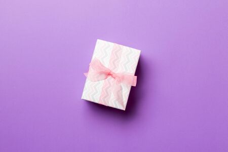 Gift box with pink bow for Christmas or New Year day on purple background, top view with copy space.