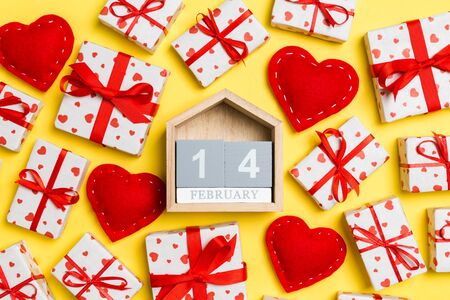 Composition of wooden calendar, holiday white gift boxes and red textile hearts on colorful...