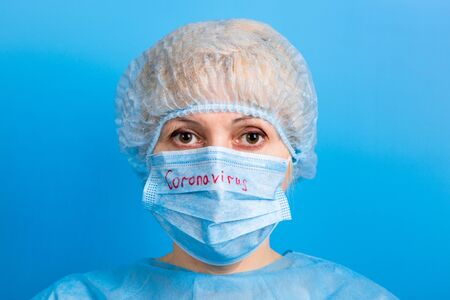 Portrait of ill woman wearing medical uniform and mask with coronavirus text at blue background. Coronavirus and health care concept.の写真素材