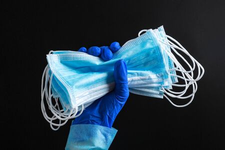 Hand in medical glove is holding a bunch of protective masks at black background. Coronavirus concept. Healthcare concept.の写真素材