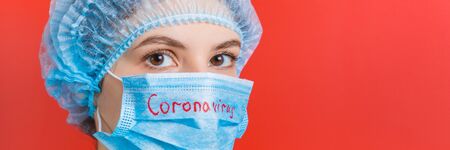 Portrait of a woman wearing medical uniform and mask with coronavirus word at red background. Coronavirus concept. Respiratory protection concept with copy space.の写真素材
