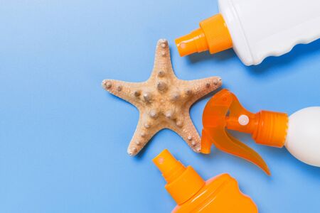 sunscreen cream with starfish and seashells in bottles on blue background, top view.
