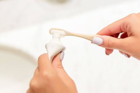Cropped image of female hands putting toothpaste on the toothbrush in the bathroom. Dental care concept. Preparation for teeth cleaning.の写真素材