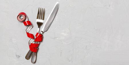 Crossed fork and knife are wrapped in measuring tape on gray background. Concept of diet for weight loss with copy space.の写真素材
