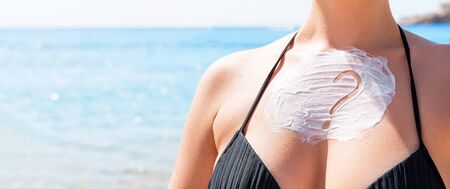 Question mark made of sun cream on woman's breast over sea background.
