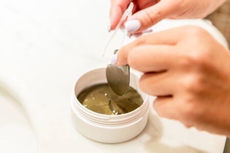 Female hands are taking eye patches out from the container with the tweezers. Anti aging concept.の写真素材