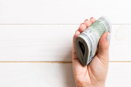 A pack of one hundred dollar bills in female hand on wooden background. Salary concept with copy...