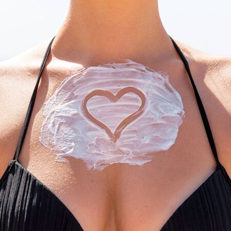Heart shaped sunblock on woman's breast at the beach. Skincare concept.