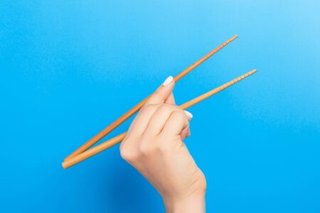 Female hand with chopsticks on blue background. Traditional asian food with emty space for your design.の写真素材