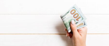 Top view of female hand holding a pack of money on wooden background. One hundred dollars. Business concept with empty space for your design. Charity and tips concept.の写真素材