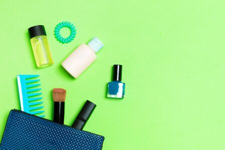 Make up products spilling out of cosmetics bag on green background with empty space for your design.の写真素材