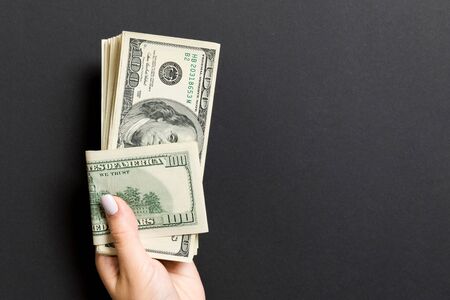 Female hand holding a bundle of one hundred dollar banknotes on colorful background. Salary and wage...
