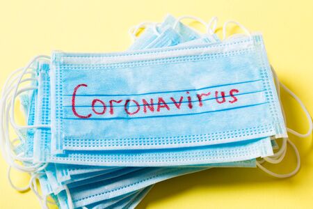 Top view of yellow background with coronavirus word on protective medical masks. Respiratory...