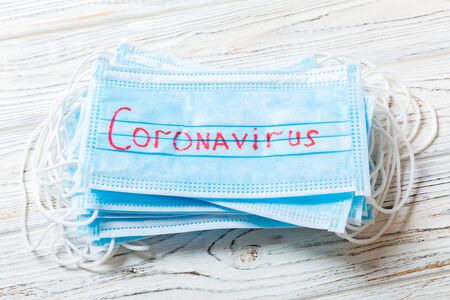 Pile of protective medical masks with coronavirus word on wooden background. Respiratory syndrome. Protect your health concept.の写真素材
