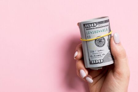 Top view of female hand holding a pack of rolled money on colorful background. One hundred dollars....