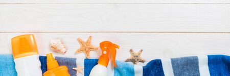 Sunscreen bottles with starfish and blue towel on white wooden table banner with copy space. Travel...