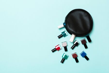 Top view of cosmetics bag with fallen out colourful nail polishes on blue background. Beautiful...
