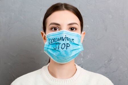 Portrait of a woman in medical mask with stop coronavirus text at gray cement background. Coronavirus concept. Respiratory protection.の写真素材