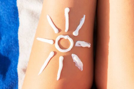 Woman sunbathing on the beach with a drawing of sun on her leg with sunscreen cream.