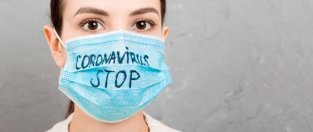 Portrait of a woman in medical mask with stop coronavirus text at gray cement background. Coronavirus concept. Respiratory protection.の写真素材