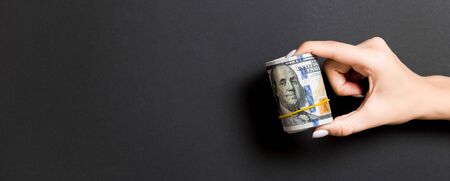 A pack of rolled one hundred dollar bills in female hand on colorful background. Salary concept with copy space.の写真素材