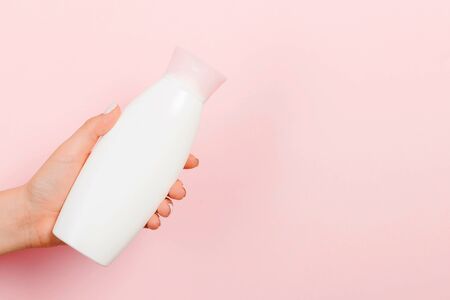Close up of female hand holding cosmetics bottle at pink background with copy space.の写真素材