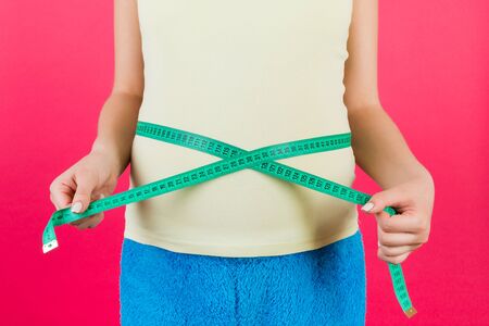 Cropped image of pregnant woman in colorful home clothing measuring her abdomen to check baby...