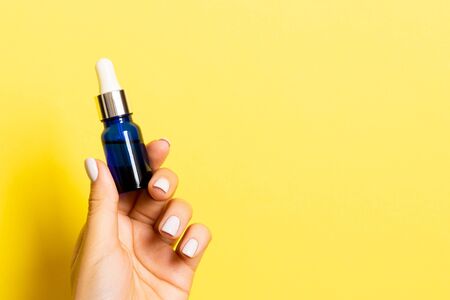 Close up of female hand holding a bottle of cosmetics product at yellow background with copy space.の写真素材