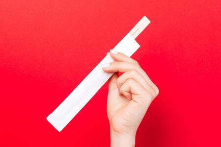 Woman's hand holding chopsticks in a pack on red background. Chinese food concept with empty space...