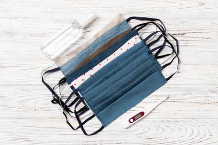 Top view of homemade cotton masks, digital thermometer and alcohol hand sanitizer on wooden background. Health care concept with copy space.の写真素材