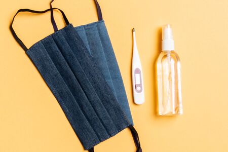 Top view of handmade cotton masks, digital thermometer and alcohol gel sanitizer on orange...
