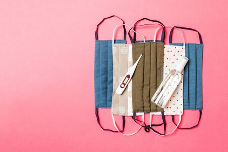 Top view of homemade cotton masks, digital thermometer and alcohol hand sanitizer on pink...