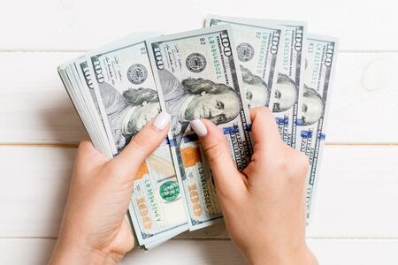 Top view of female hands counting money. One hundred dollar banknotes on wooden background. Business...