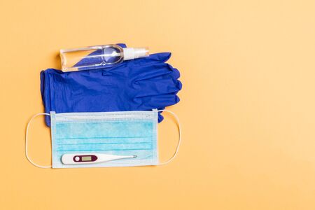 Top view of alcohol hand sanitizer, latex gloves, digital thermometer and medical mask on orange background. Virus protection equipment concept with copy space.の写真素材