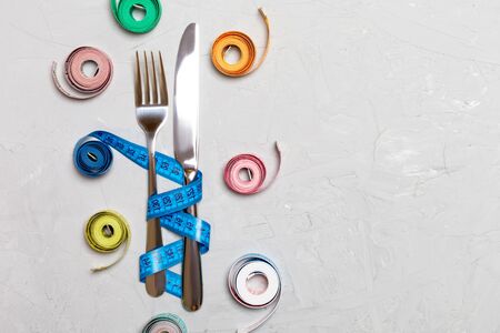 Composition of colored measuring tapes, fork and knife on cement background with empty space for your design. Overweight concept.の写真素材