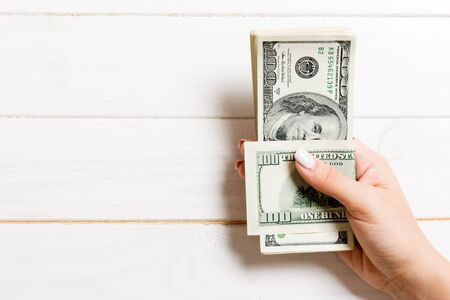 Female hand holding a bundle of one hundred dollar banknotes on wooden background. Salary and wage...