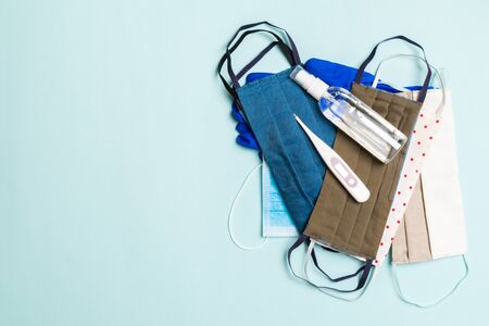 Top view of homemade cotton masks, digital thermometer and alcohol hand sanitizer on blue...