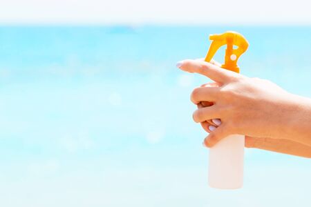 Croped image of woman's hand holding sunscreen spray at the sea background.の写真素材