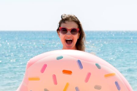 Beautiful young woman is posing with a doughnut inflatable ring at the sea background.の写真素材