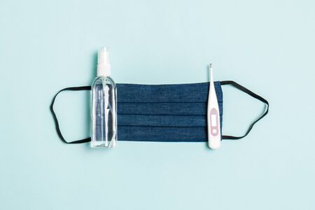 Top view of handmade cotton mask, alcohol hand sanitizer and digital thermometer on blue background with copy space. Protective medical equipment concept.の写真素材