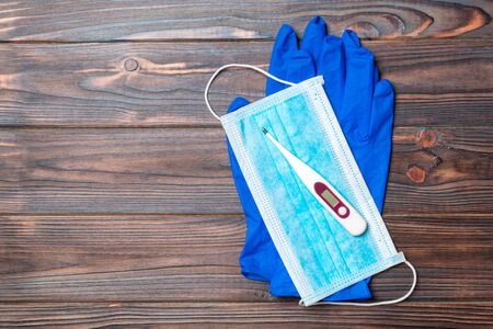 Top view of medical gloves, digital thermometer and surgical mask on wooden background with copy...