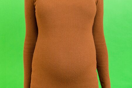 Cropped image of pregnant woman's abdomen at green background. Future mother is wearing brown dress....