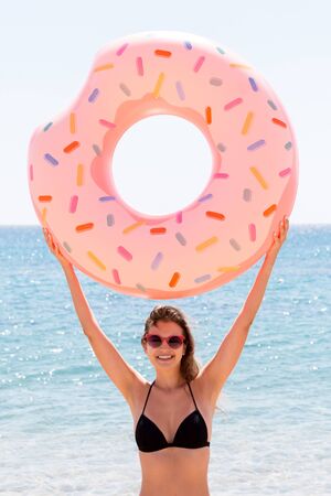 Beautiful woman is playing with donut rubber ring on the beach at the sea background.の写真素材