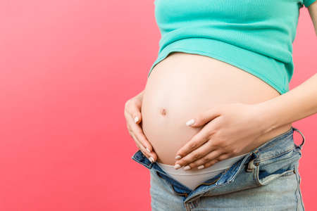 Close up of pregnant woman in unzipped jeans showing her naked abdomen at colorful background with copy space.の写真素材