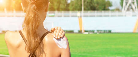 Fitness woman is applying sunscreen on her shoulder before training at the stadium. Protect your...