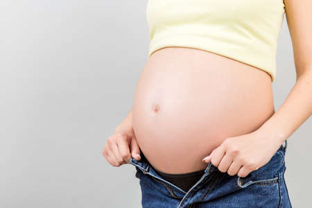 Close up of pregnant woman in unzipped jeans showing her naked abdomen at colorful background with copy space.の写真素材