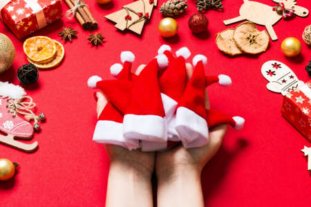 Top view of female hands holding a stack of santa hats on red background. New year decorations....