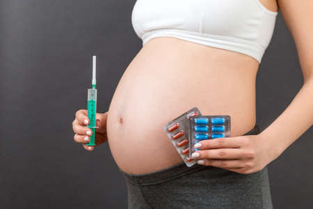 Close up of pregnant woman holding a syringe and blisters with pills. A choice between injection and medications concept.の写真素材