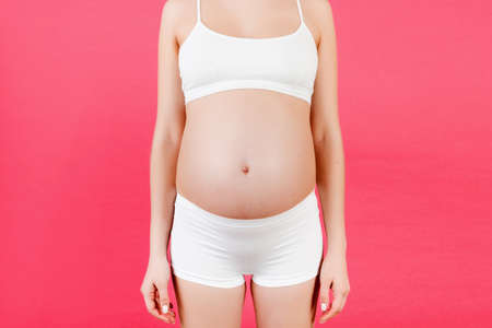 Cropped image of pregnant woman's belly at blue background. Future mom in white underwear. Parenthood concept. Copy spaceの写真素材
