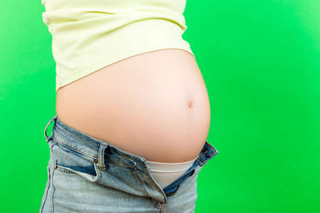 Close up of expecting mother in unzipped jeans showing her naked pregnant belly at colorful background with copy space. Pregnancy concept.の写真素材